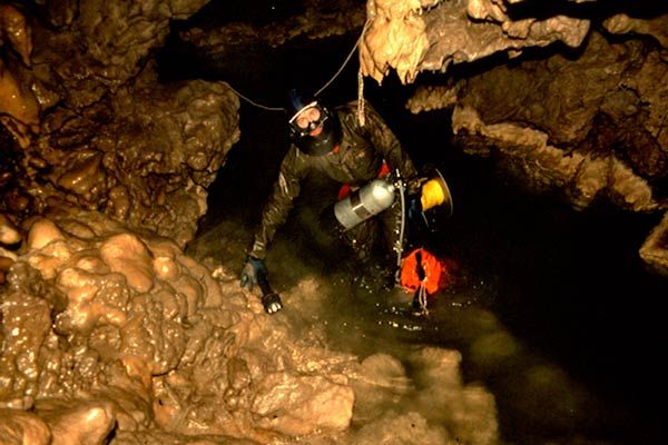 Cave diver entering flooded siphon at the Grotto in Rat's Nest Cave, Canmore Alberta — cave diving exploration of submerged passages in Canadian Rockies cave system